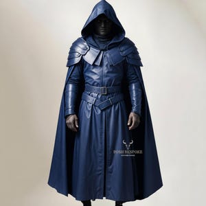 Puede incluir: Una capa con capucha azul oscuro con armadura en los hombros y un cinturón. La capa tiene un diseño largo y fluido y está hecha de un material similar al cuero. La imagen incluye el texto "POSH BESPOKE LEATHER GOODS".