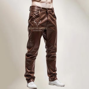 Op de afbeelding: Bruine leren broek met een slanke pasvorm. De broek heeft een riemlusband en een rits. De merknaam "POSH BESPOKE LEATHER GOODS" staat op de voorkant van de broek.