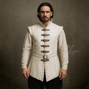 May include: Cream-colored leather vest with a high collar and multiple brown leather straps. The vest is worn over a long-sleeved shirt. The garment has a medieval or renaissance style.