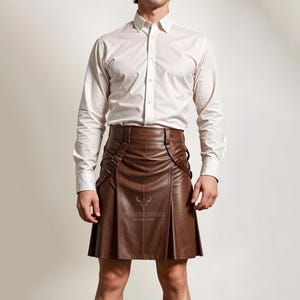 Pode incluir: Um kilt de couro marrom com fivelas e correias. O kilt &eacute; usado com uma camisa branca de bot&otilde;es.