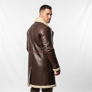May include: A brown leather coat with a cream-colored shearling collar and cuffs. The coat is knee-length and features a button closure and a split in the back. The text "POSH BESPOKE LEATHER GOODS" is visible on the coat.