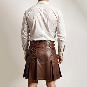 Pode incluir: Um kilt de couro marrom com pregas e correias ajust&aacute;veis. O kilt &eacute; usado com uma camisa branca de bot&otilde;es.