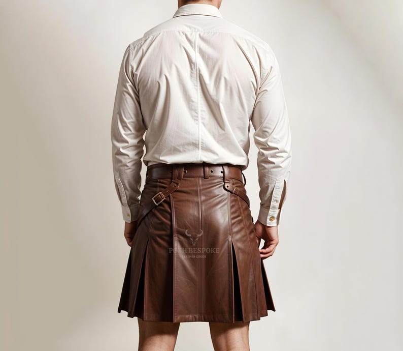 Pode incluir: Um kilt de couro marrom com pregas e correias ajust&aacute;veis. O kilt &eacute; usado com uma camisa branca de bot&otilde;es.