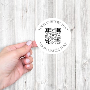 May include: White round sticker with a black and white QR code in the center. The text "YOUR CUSTOM TEXT" is printed around the QR code.