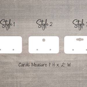 May include: Three styles of white earring display cards with holes for earrings. The cards measure 2.5 cm high by 5 cm wide. "Cards Measure 1" H x 2" W" is printed below the cards.