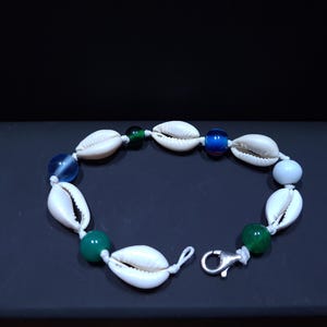 Könnte beinhalten: Ein Armband aus weißen Muscheln mit blauen und grünen Glasperlen und einem silbernen Verschluss.