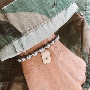 May include: A silver beaded bracelet with a silver dog tag charm featuring a small heart engraved on it.