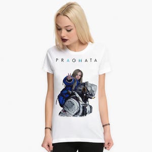 May include: A white short-sleeved t-shirt featuring the text PRAGMATA in black letters with blue accents. The graphic depicts a young person with long blonde hair wearing a blue jacket, reaching out with one hand while sitting on a large robot.