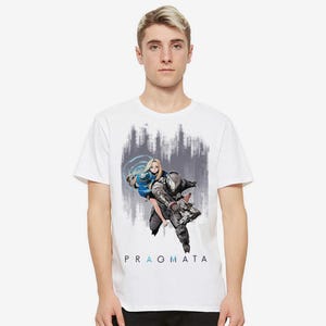 May include: A white short-sleeve t-shirt featuring a graphic print of a blonde character and a futuristic armored figure in motion. The design includes a blue circular energy effect and the text PRAGMATA in black and blue lettering centered below.