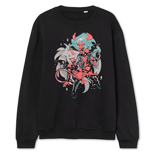 May include: Black sweatshirt featuring a colorful graphic of two anime-style characters with horns, tails, and wings. The artwork includes shades of red, teal, and white, set against a black background. The design has a cartoonish style.