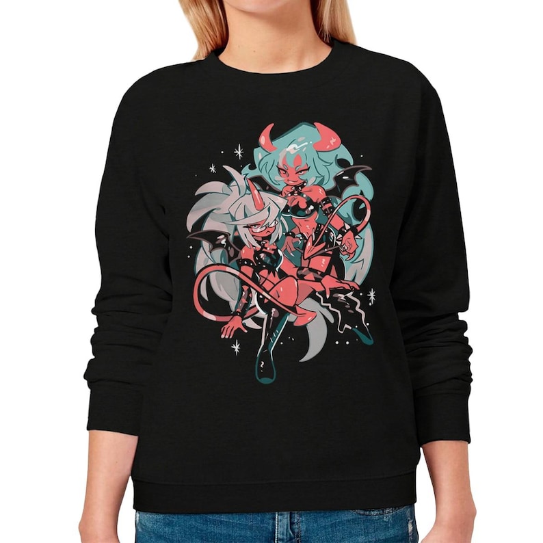 May include: Black sweatshirt featuring a colorful anime-style illustration of two female characters with horns, wings, and devilish attire. The artwork includes red, pink, and teal accents, set against a white background with star details.