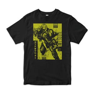 May include: A black short-sleeved t-shirt featuring a lime green rectangular graphic. The print depicts a character carrying another, with text including "DIANA 03367", "PRAGMATA", "24 APRIL 2026", "HUGH FATHER", and Japanese characters in a distressed style.