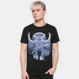 May include: Black t-shirt featuring a graphic print of a person standing in front of a large, white, winged figure. The figure is surrounded by a halo of light.