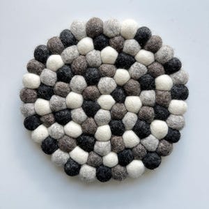 May include: A round, grey, white and black felt coaster made of small, round balls. The coaster is ideal for protecting surfaces from heat.