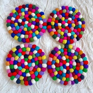 Puede incluir: Cuatro posavasos redondos de fieltro de colores hechos de pequeñas bolas de lana en varios colores, incluyendo rojo, azul, verde, amarillo, rosa, morado y blanco.