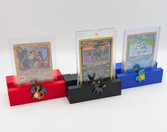 Può includere: Tre porta carte Pokémon, ognuno con una base di colore diverso e una figura di Pokémon. Il porta carte rosso ha una figura di Charizard, il porta carte nero ha una figura di Umbreon e il porta carte blu ha una figura di Blastoise. Ogni porta carte ha una fessura in plastica trasparente per una carta Pokémon.