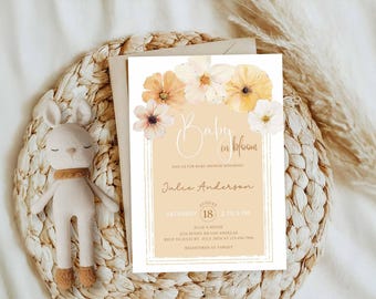 May include: A baby shower invitation with floral accents and the text "Baby in Bloom." The invitation features a cream-colored background with a decorative border and is adorned with watercolor flowers in shades of peach, yellow, and white. A stuffed bunny is next to the invitation.
