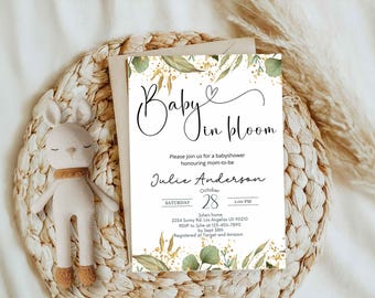May include: A baby shower invitation with the words "Baby in Bloom" in elegant script, adorned with botanical illustrations. A plush bunny toy with a tan scarf rests beside the invitation on a woven mat.