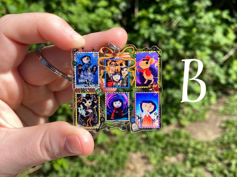 May include: A clear acrylic keychain featuring six colorful postage stamp designs with characters from a movie. The keychain has a silver-colored ring and a green and gold bow. The letter "B" is visible in the background.