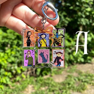 May include: A clear acrylic keychain featuring a collage of six colorful postage stamp designs. Each stamp depicts a character from a movie. The keychain has a silver-colored metal ring and clasp.