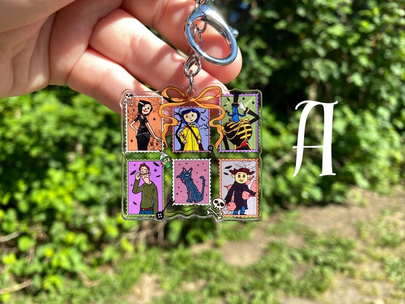 May include: A clear acrylic keychain featuring a collage of six colorful postage stamp designs. Each stamp depicts a character from a movie. The keychain has a silver-colored metal ring and clasp.