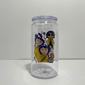 May include: Clear plastic tumbler with a lid, featuring a colourful graphic of characters from the animated film "Coraline." The design includes illustrations of the main character and other elements from the movie.