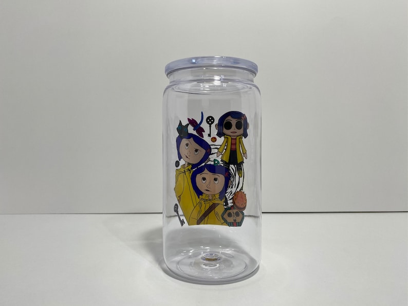 May include: Clear plastic tumbler with a lid, featuring a colourful graphic of characters from the animated film "Coraline." The design includes illustrations of the main character and other elements from the movie.
