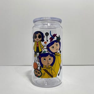 May include: Clear plastic tumbler with a lid, featuring a colourful graphic of three cartoon characters in yellow coats and blue hair. The design includes a key, dragonfly, and other decorative elements.