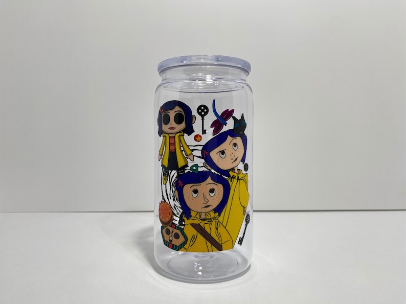 May include: Clear plastic tumbler with a lid, featuring a colourful graphic of three cartoon characters in yellow coats and blue hair. The design includes a key, dragonfly, and other decorative elements.