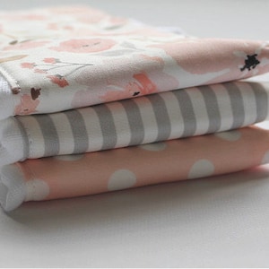 May include: A stack of four fabric squares in pink, white, and gray. The top square has a floral pattern, the second square has gray and white stripes, the third square has white polka dots on a pink background, and the bottom square is white.
