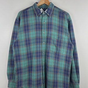 May include: A long-sleeved button-down shirt featuring a plaid pattern in shades of teal, dark blue, and muted brown. The shirt includes a standard collar, a single chest pocket on the left side, and a buttoned front placket with light-coloured buttons.
