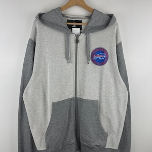 Pode incluir: Um casaco com capuz e fecho de correr em cinzento claro e escuro, com um emblema do logótipo dos Buffalo Bills no lado esquerdo do peito. A peça inclui um capuz com cordão, um fecho de correr frontal a todo o comprimento e dois bolsos frontais.