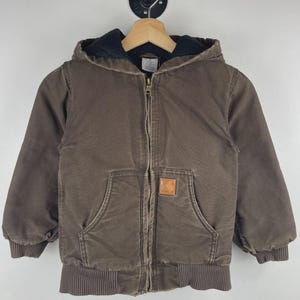 May include: A brown hooded jacket with a full-length metal front zip, long sleeves with ribbed cuffs, and a ribbed hem. The jacket features a dark interior lining, a quilted texture, and a small rectangular tan brand patch on the front pocket.