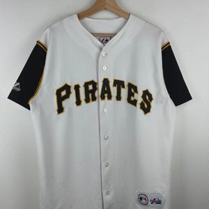 May include: A white baseball jersey with black sleeves and yellow trim. The word PIRATES is embroidered in black with yellow outlines across the chest. It features a button-down front, a Majestic logo on the right sleeve, and a team patch at the hem.