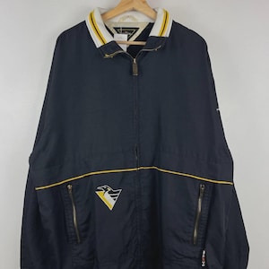 May include: A navy blue zip-up windbreaker jacket featuring a white, yellow, and black penguin logo on the chest. The jacket has a ribbed collar with yellow and white stripes, two zippered front pockets, and a full-length front zipper closure.