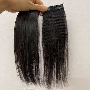 Op de afbeelding: Twee zwarte haarextensions worden tegen een witte achtergrond gehouden. De ene extension is glad, de andere heeft een gekreukte textuur. Beide hebben een zwarte clip aan de bovenkant.