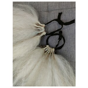 May include: Two long, white hair extensions with black ties. The extensions are tied together with a black ribbon.