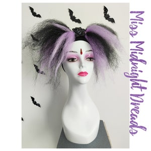 Può includere: Una parrucca nera e viola con due lunghe code di cavallo ricciute. La parrucca è decorata con un cerchietto nero e una rosa nera.