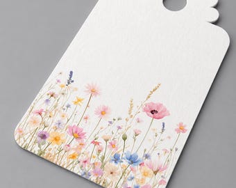 May include: A white rectangular gift tag with a scalloped top edge and a circular hole. The bottom portion features a watercolor illustration of a wildflower meadow with various small flowers in shades of pink, yellow, blue, and purple.