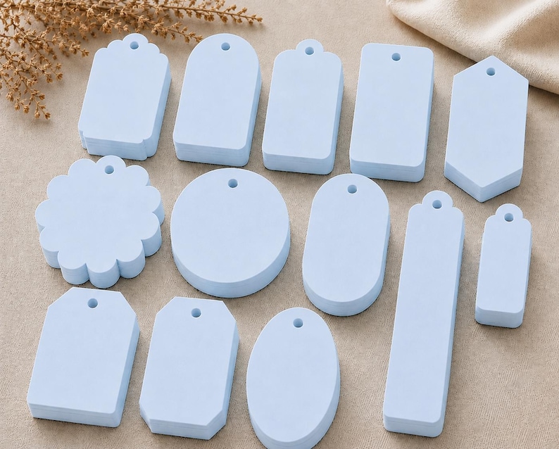 May include: A collection of thirteen light blue tags in various geometric shapes, including circles, rectangles, ovals, and scalloped edges. Each tag features a single pre-punched hole at the top, providing a uniform look for labeling or crafting projects.