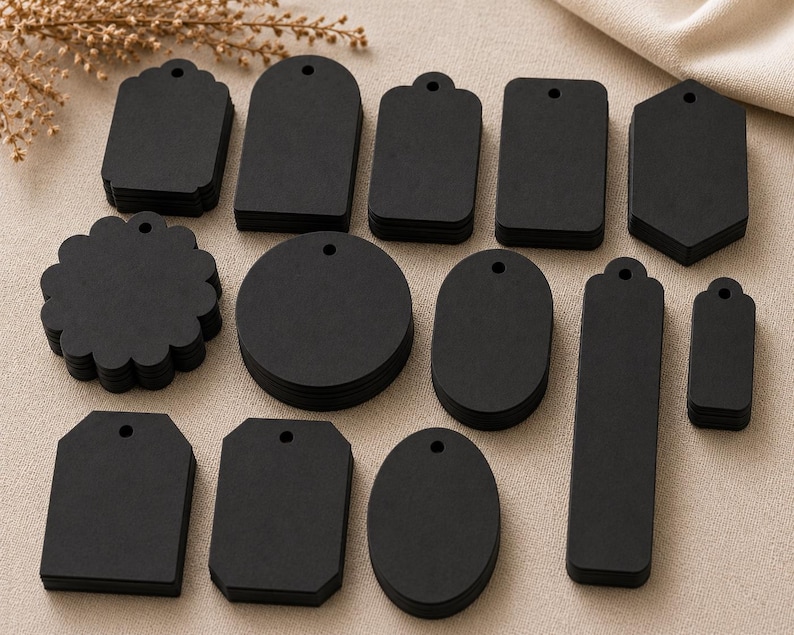 May include: A collection of black paper tags in various shapes including circles, rectangles, ovals, and scalloped edges. Each tag features a single pre-punched hole at the top for stringing. The set includes multiple stacks of uniform shapes.