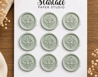 May include: A white rectangular display card labeled Starlace Paper Studio and WAX SEALS featuring nine circular sage green wax seals arranged in a three-by-three grid, each embossed with a detailed fleur-de-lis design in the center.