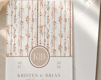 May include: A wedding invitation card featuring a vertical pattern of hanging floral vines in shades of peach, brown, and sage green. A central circular emblem displays the initials KB, with the date 10 17 20 26 and the names Kristen & Brian printed below.
