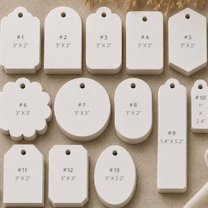 May include: A collection of thirteen white paper tags in various shapes, including rectangular, circular, oval, and scalloped designs. Each tag features a pre-punched hole at the top and is labeled with a number and its specific dimensions in inches.
