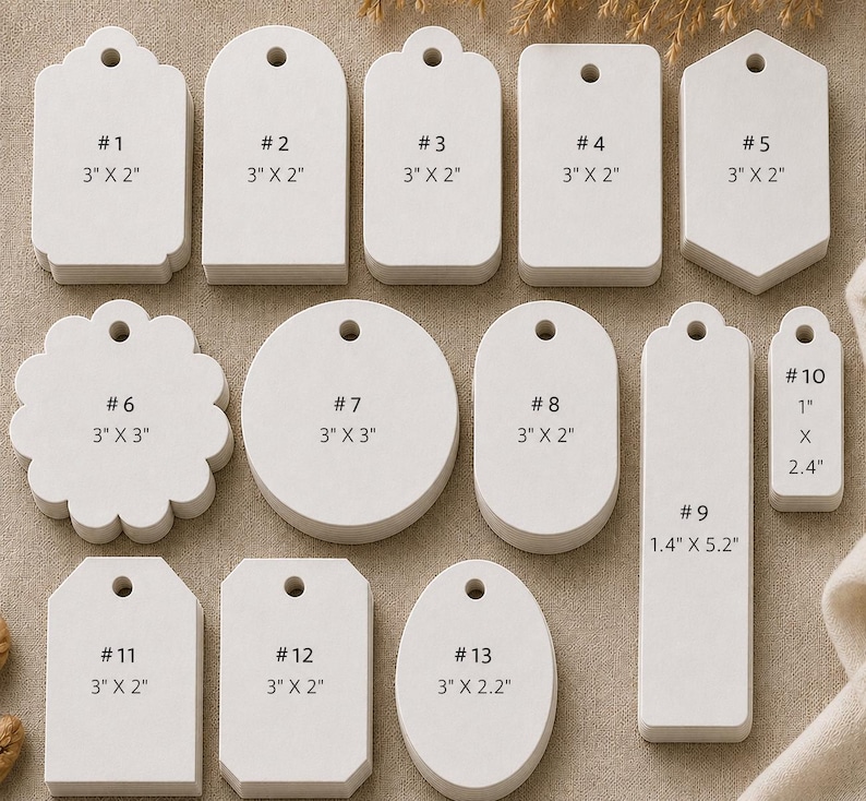 May include: A collection of thirteen white paper tags in various shapes, including rectangular, circular, oval, and scalloped designs. Each tag features a pre-punched hole at the top and is labeled with a number and its specific dimensions in inches.