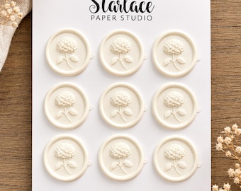 May include: A white card featuring the text Starlace PAPER STUDIO and WAX SEALS, displaying nine circular off-white wax seals arranged in a three-by-three grid. Each wax seal features a raised, detailed embossed design of a hydrangea flower.