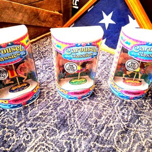 May include: Three Carousel Classics die-cast metal toys in clear plastic containers. Each toy features a miniature carousel with a horse and a colorful base. The containers have the names Brittany, Dawn, and Carrington.
