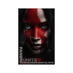 May include: A movie poster featuring a close-up of a person's face with red paint across the face. The text "PANEM" is vertically stacked on the left side. Below, the text reads "UNITE 013" and "THE REVOLUTION IS ABOUT ALL OF US."