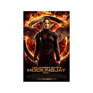 May include: Movie poster for The Hunger Games: Mockingjay Part 1, featuring Jennifer Lawrence as Katniss Everdeen in a fiery, dystopian setting. The poster features the Mockingjay symbol and the text "The Hunger Games: Mockingjay Part 1" and "November 21".