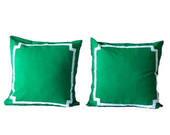 May include: Two green throw pillows with white trim. The pillows have a simple, square shape and a solid green color.